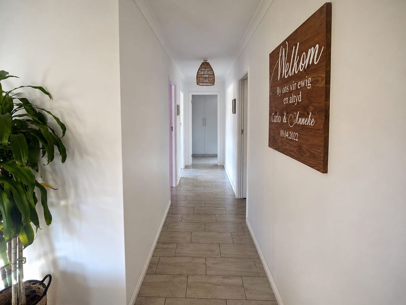A clean, well-maintained hallway featuring neutral tiled flooring, crisp white walls, and a central pendant light fixture leading to adjacent rooms.