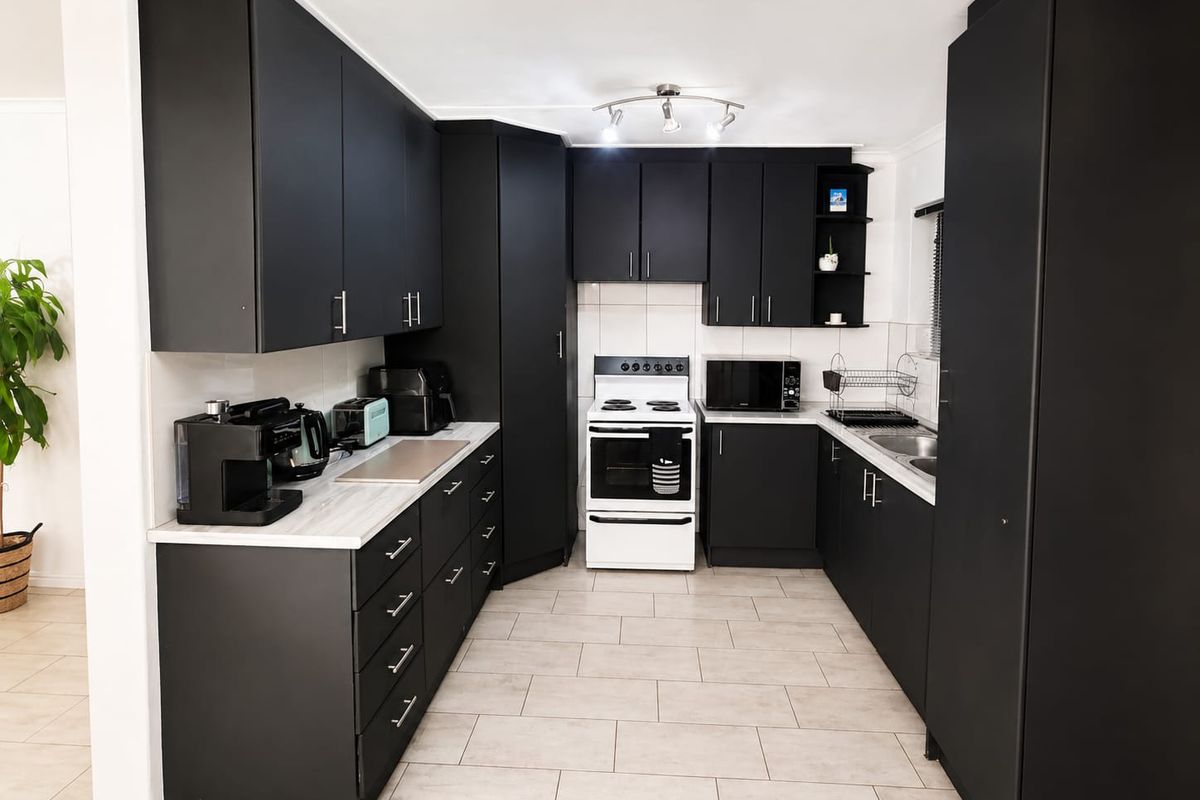 Modern kitchen featuring matte black cabinetry, light-toned laminate countertops, tiled flooring, and a freestanding stove, offering a clean and contemporary aesthetic.