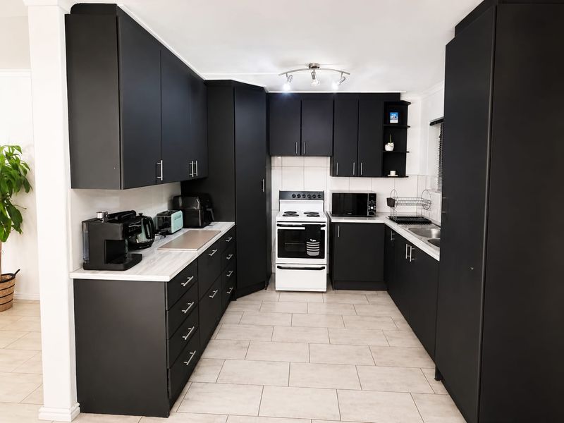 Modern kitchen featuring matte black cabinetry, light-toned laminate countertops, tiled flooring, and a freestanding stove, offering a clean and contemporary aesthetic.