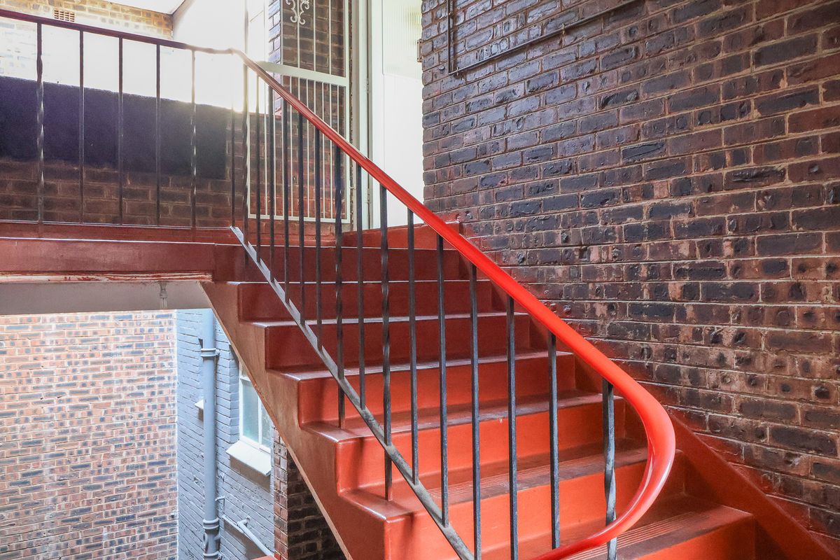 Exterior view of a brick apartment building featuring a painted metal staircase and security gate access.