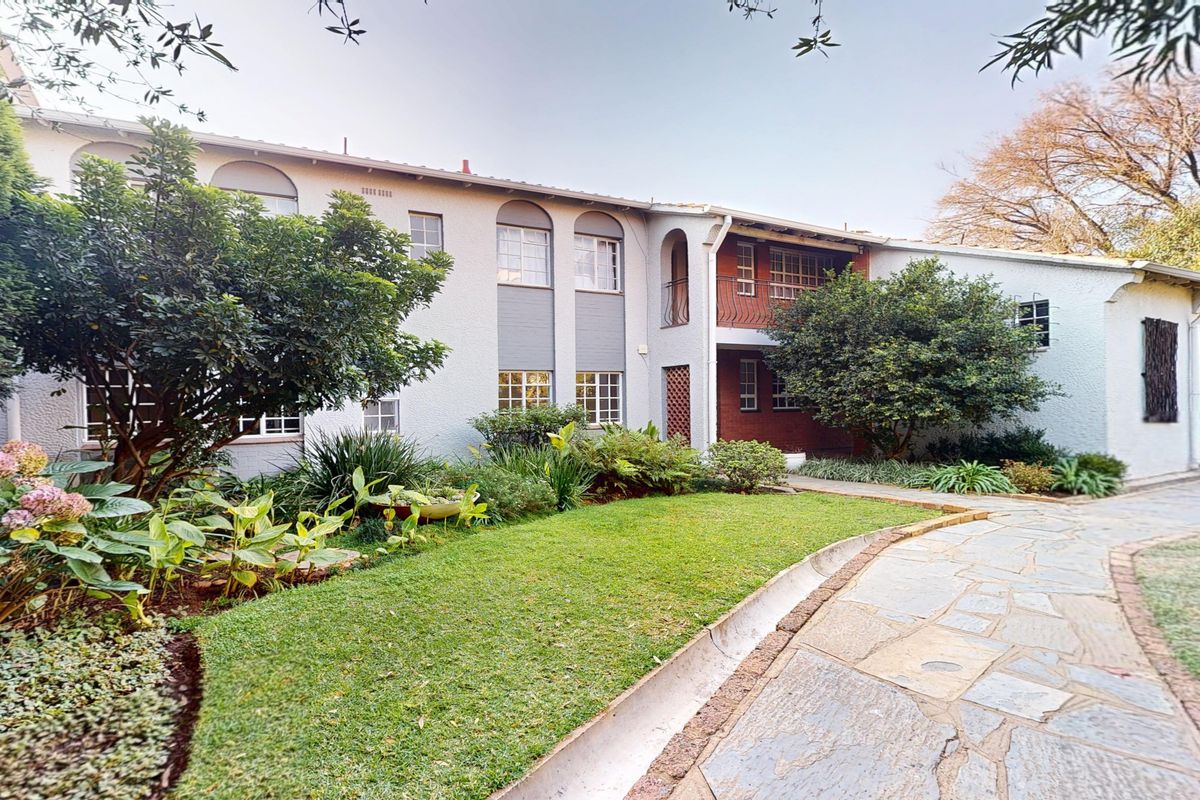 A well-maintained rear exterior view featuring a stone paved walkway, lush garden landscaping, and a charming two-story facade with arched architectural details.