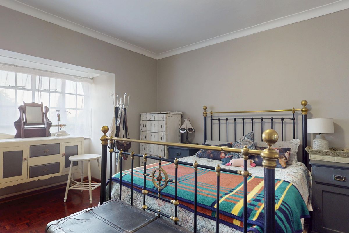 A well-proportioned bedroom featuring classic parquet flooring, neutral wall tones, and a large multi-pane window that provides ample natural light.