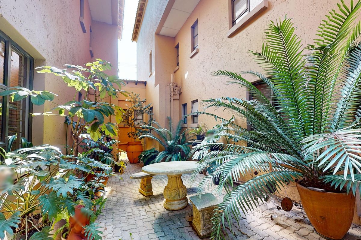 A private paved courtyard area situated between townhouse building sections, featuring textured exterior walls and established garden greenery.
