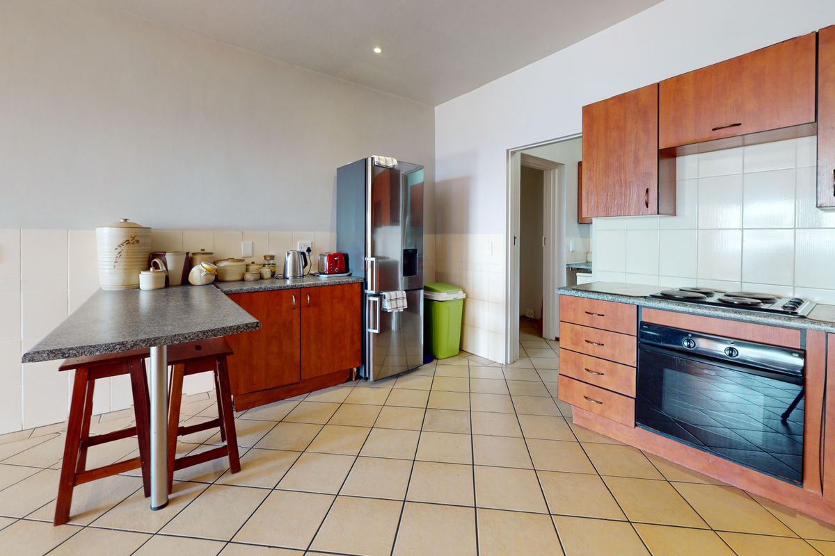 A functional kitchen featuring wood-finish cabinetry, laminate countertops, a built-in oven with hob, and a breakfast bar area with tiled flooring.