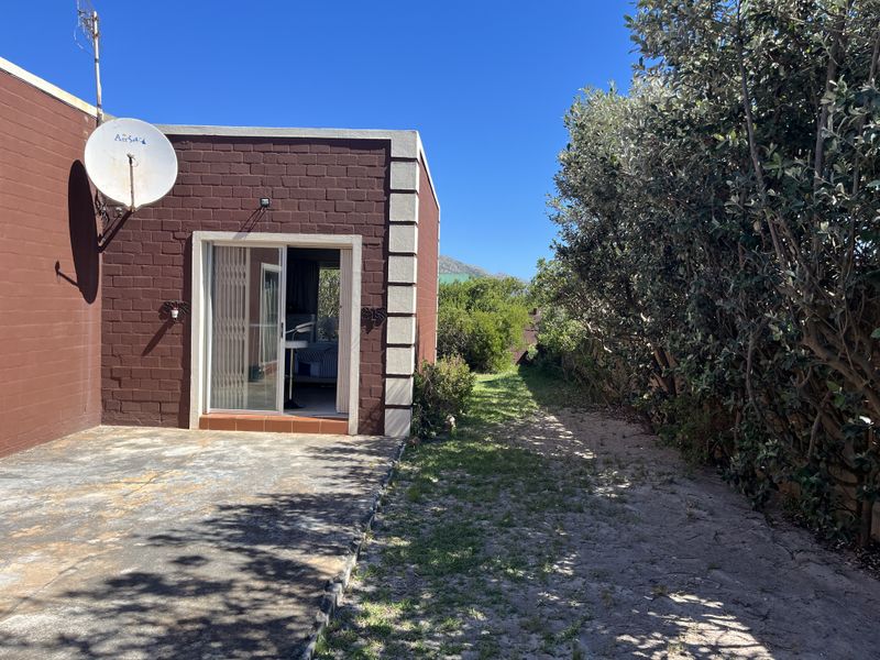 Rear exterior view of the property featuring a concrete patio, sliding glass door access, and a private garden area with mature hedging.