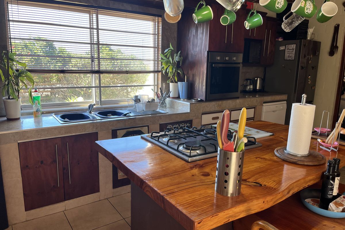 A functional kitchen featuring a timber-topped island with a gas hob, double sink, built-in oven, and ample cabinetry with tiled flooring.