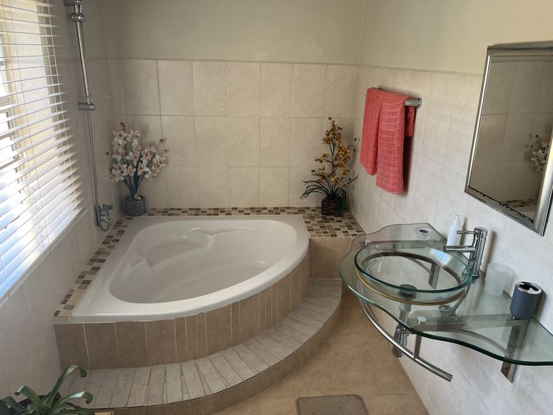 A compact bathroom featuring a corner bathtub with tiled surround, a modern glass vessel sink, and neutral wall tiling.