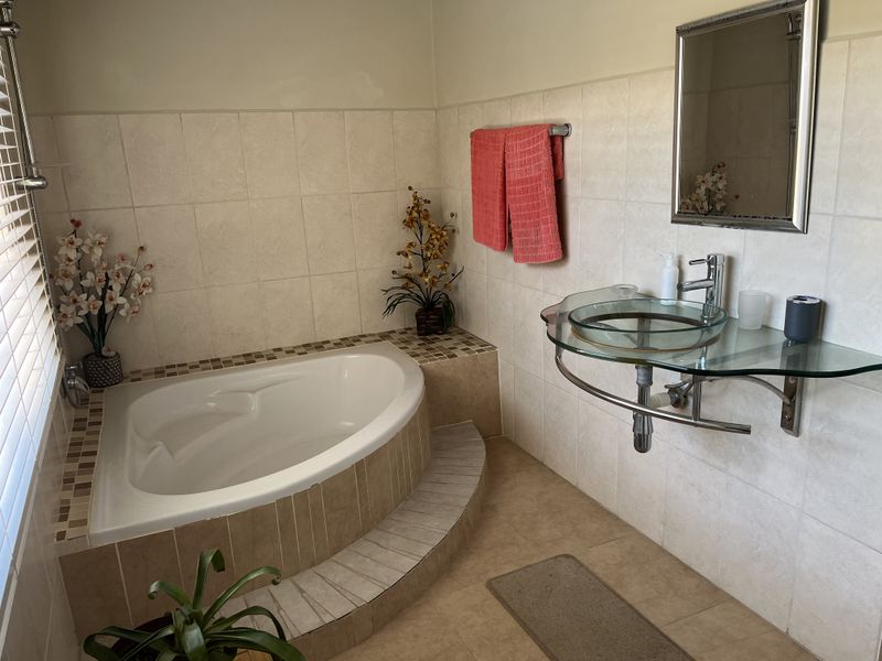 A bathroom featuring a built-in corner bathtub with tiled surround and a modern glass vessel sink with wall-mounted chrome fixtures.