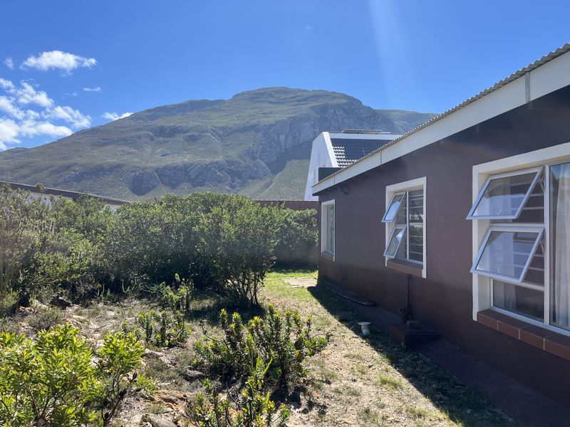 Rear exterior view of the property featuring a brown facade, aluminium windows, and a garden area with mountain views.