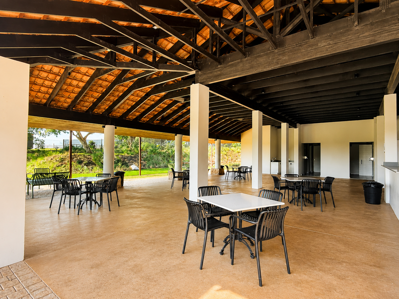 A spacious covered outdoor patio featuring exposed timber roof trusses, concrete flooring, and structural columns, ideal for large-scale outdoor entertaining.