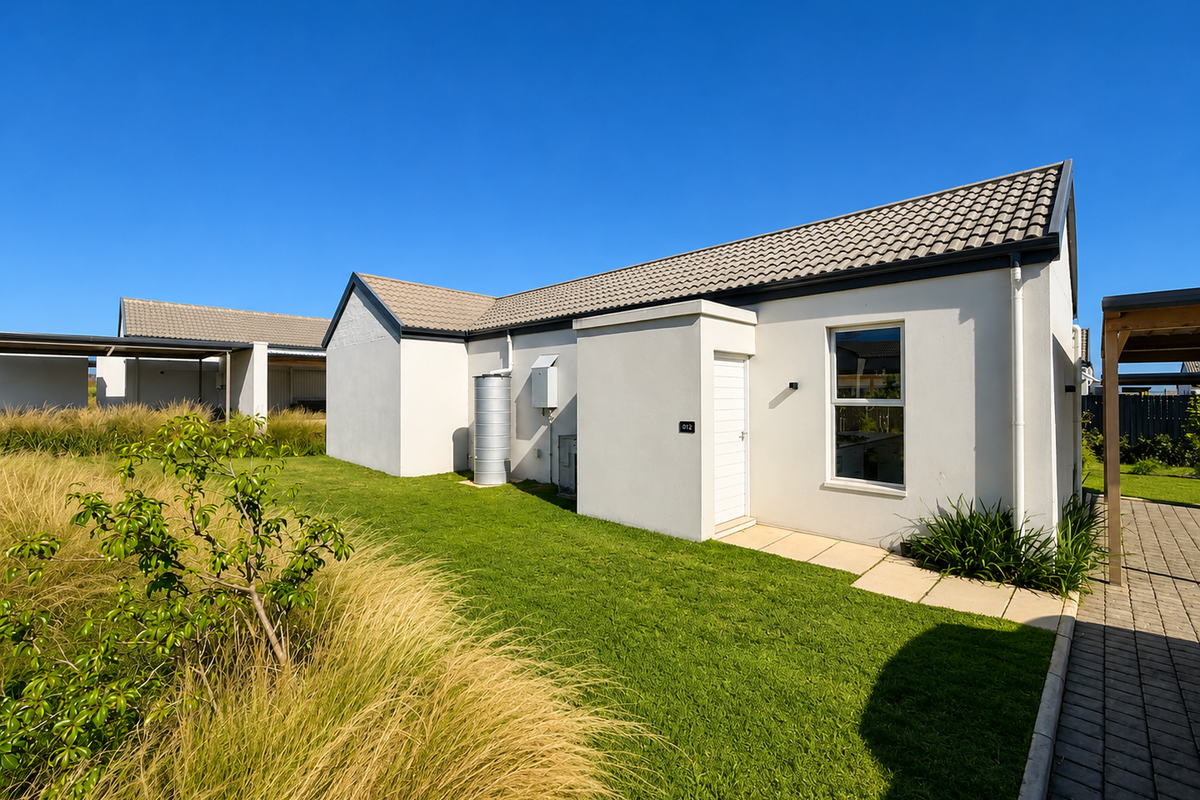 A well-maintained rear exterior view of a modern house featuring a paved walkway, landscaped lawn, and a water tank.