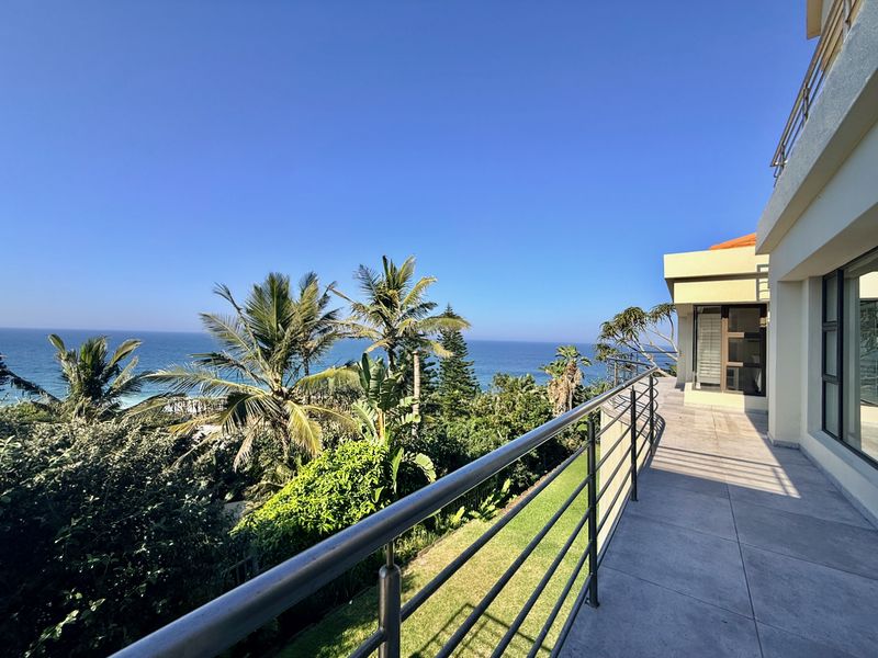 Spacious balcony featuring modern tiled flooring and a stainless steel balustrade, offering expansive ocean views and direct access to the home.
