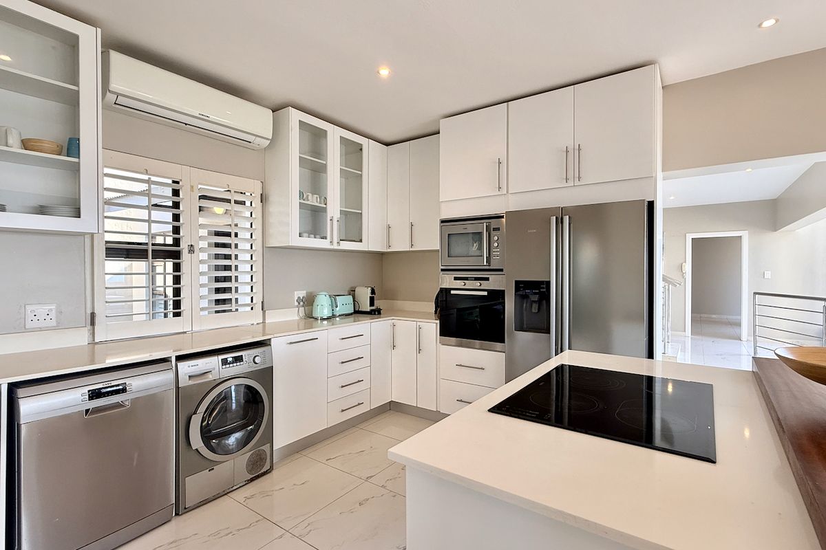Modern kitchen featuring white cabinetry, stone countertops, integrated appliances, induction cooktop, and tiled flooring with plantation shutters.