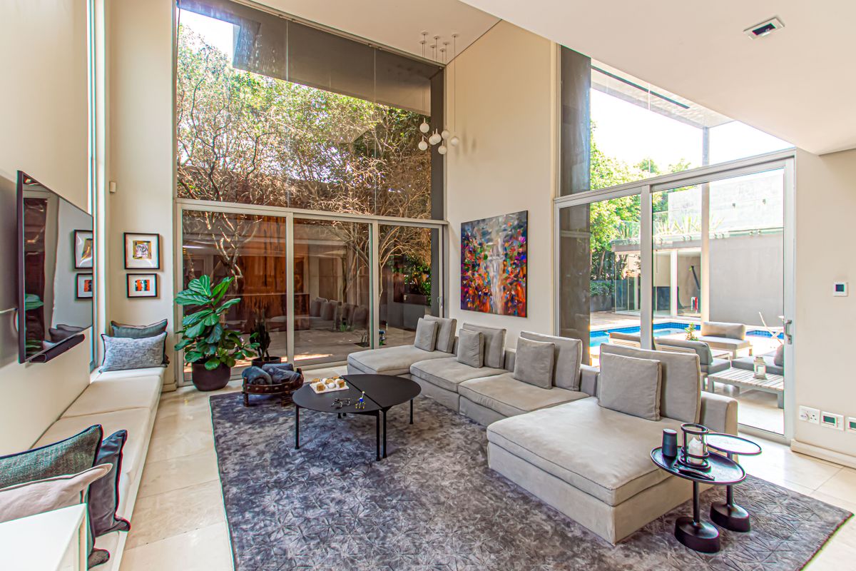 Spacious double-volume living room featuring floor-to-ceiling glass walls, stone flooring, and seamless indoor-outdoor flow to the pool area.