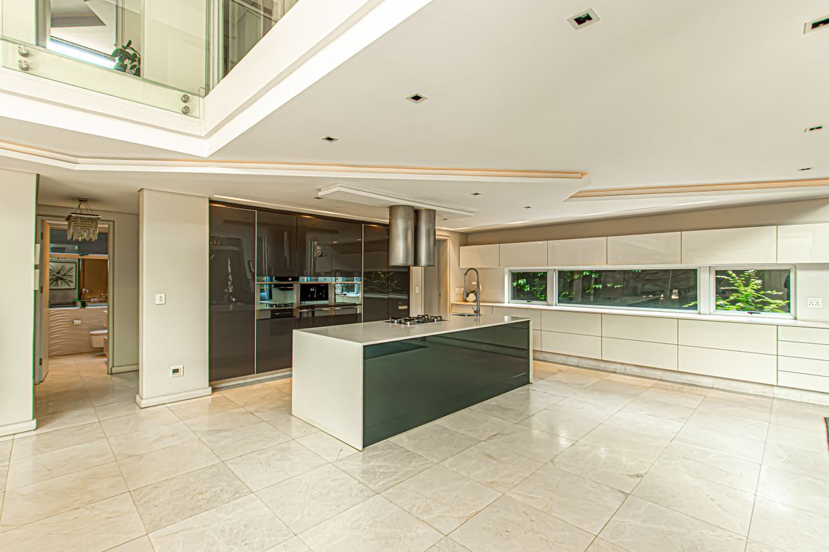 Modern, spacious kitchen featuring a central island with gas hob, high-gloss cabinetry, integrated appliances, and sleek stone flooring in an open-plan layout.