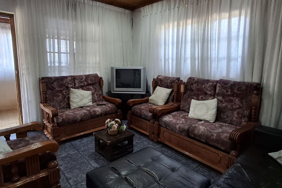 A living room featuring a timber-clad ceiling with a central fan and dark tiled flooring, offering a dated aesthetic ready for modernization.