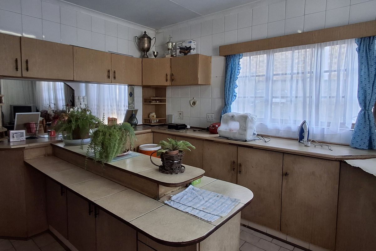 A dated kitchen featuring original laminate cabinetry, tiled countertops, and a tiled backsplash, offering significant potential for a modern renovation.