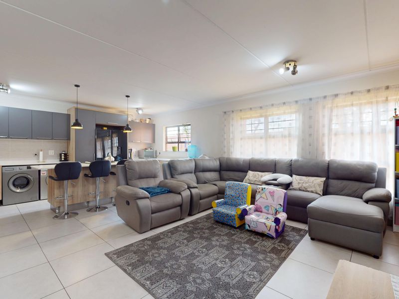 Spacious open-plan living area featuring a modern kitchen with built-in cabinetry, breakfast bar, and integrated laundry appliances, seamlessly flowing into the lounge space.