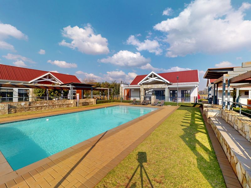 A well-maintained communal pool area featuring a paved deck, stone-clad retaining walls, and pergola structures set against a backdrop of residential buildings.