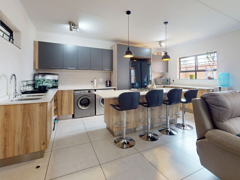 Modern open-plan kitchen featuring wood-grain and grey cabinetry, stone countertops, a central island with breakfast bar, and integrated laundry appliances.