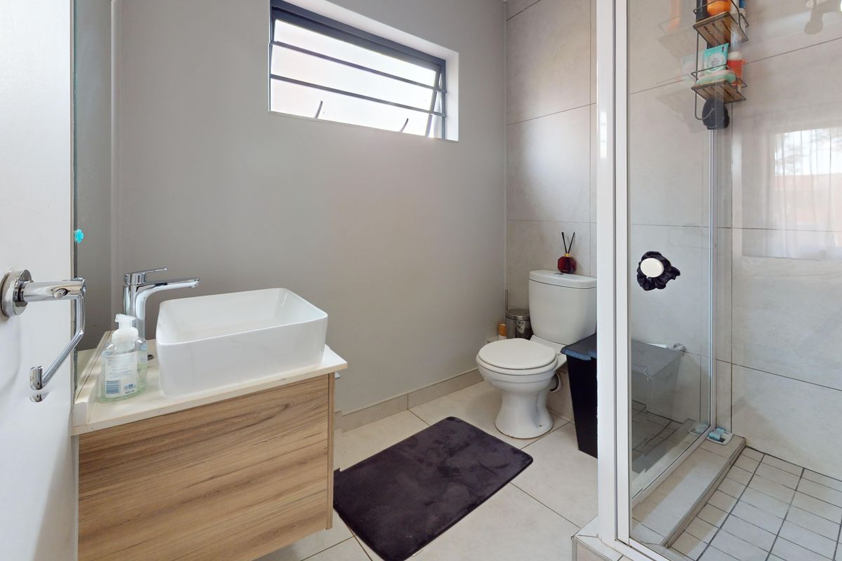 Modern bathroom featuring a vessel sink on a wood-finish vanity, a toilet, and a glass-enclosed shower with tiled walls and flooring.