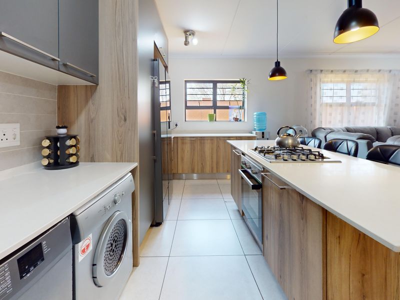 Modern open-plan kitchen featuring wood-finish cabinetry, stone countertops, a gas hob, built-in oven, and integrated laundry space, flowing into the living area.