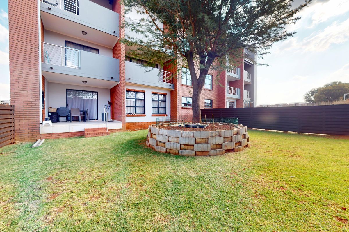Rear view of a multi-story apartment building featuring brick facade, private balconies, and a landscaped garden area with a central tree.