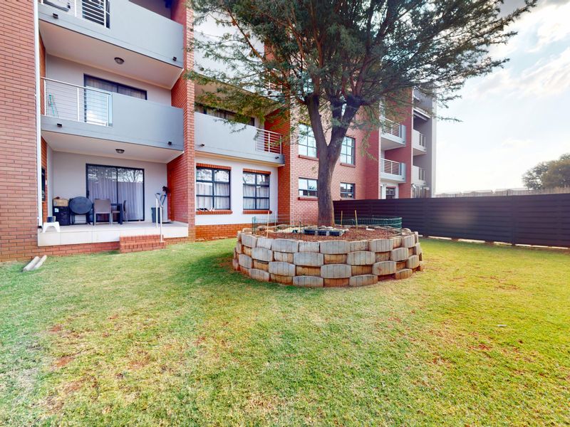 Rear view of a multi-story apartment building featuring brick facade, private balconies, and a landscaped garden area with a central tree.