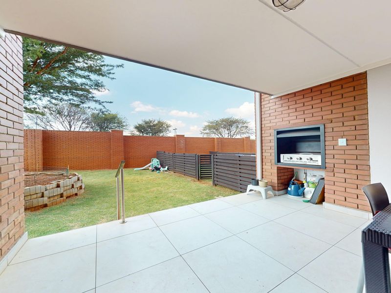 A covered patio featuring a built-in braai, tiled flooring, and direct access to a private garden area with brick boundary walls.