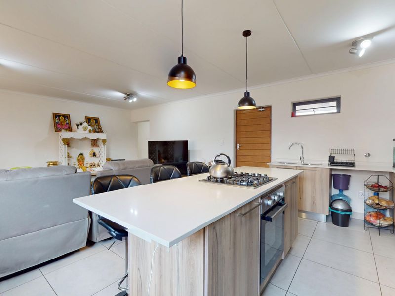 Modern open-plan living area featuring a central kitchen island with gas hob, built-in oven, and sleek cabinetry, seamlessly integrated with the living space.