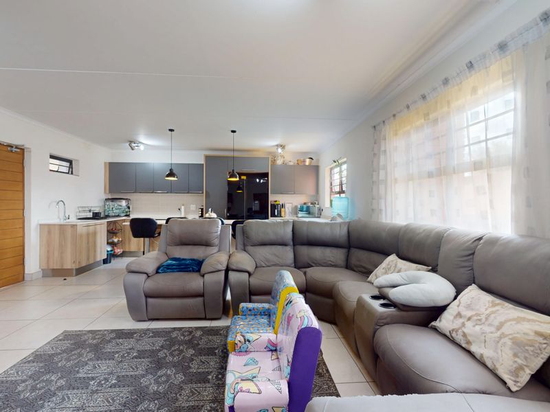 Spacious open-plan living area featuring tiled floors, a modern kitchen with built-in cabinetry, and ample natural light from large windows.