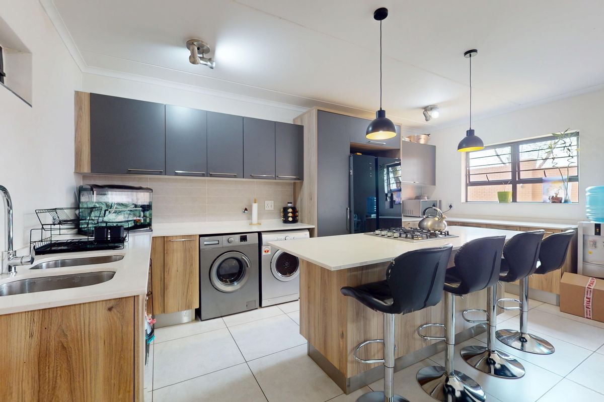 Modern kitchen featuring two-tone cabinetry, a central island with a gas hob, integrated laundry appliances, and tiled flooring.