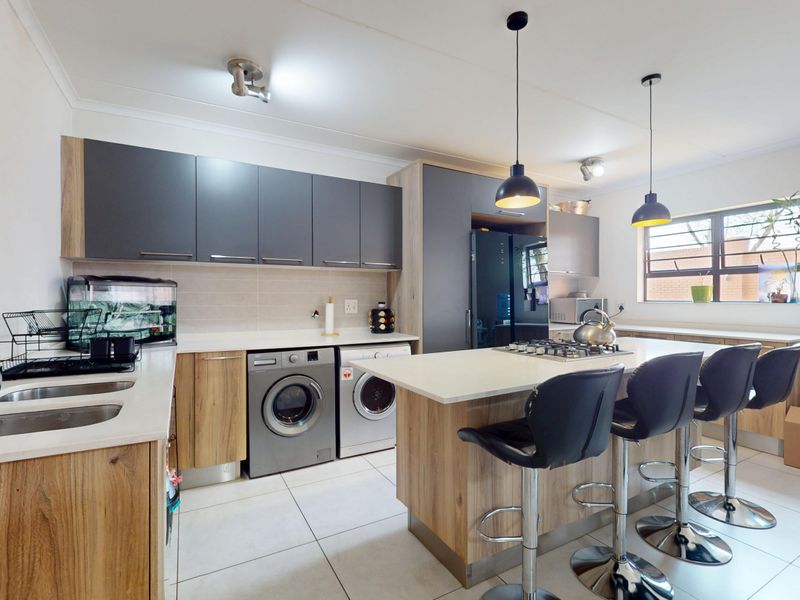 Modern kitchen featuring two-tone cabinetry, a central island with a gas hob, integrated laundry appliances, and tiled flooring.
