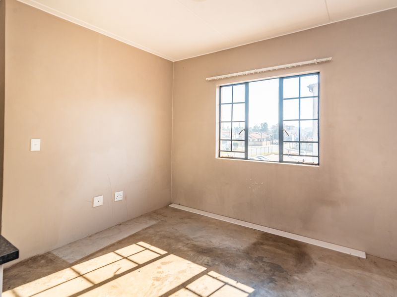 An empty bedroom featuring a steel-framed window, neutral wall paint, and concrete flooring, offering a blank canvas for renovation or interior design.