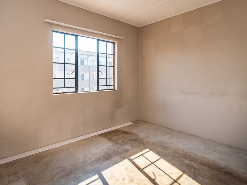 An empty bedroom featuring unfinished plaster walls and concrete flooring, awaiting final finishes and flooring installation.