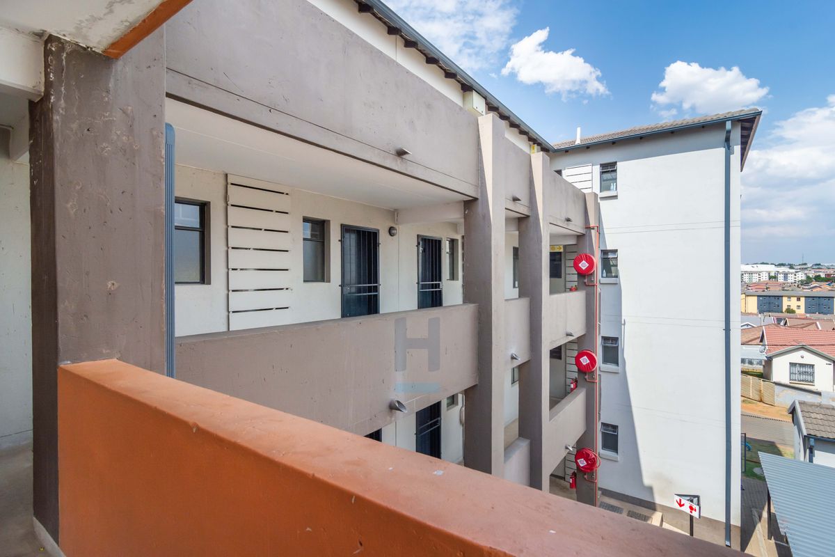 Exterior view of a multi-story townhouse complex featuring concrete walkways, security gates, and mounted fire safety equipment.