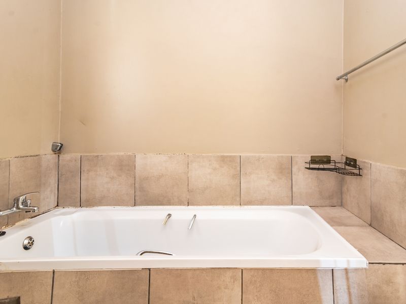 A functional bathroom featuring a built-in bathtub with chrome fixtures and neutral tiled splashback, providing a clean and simple space.