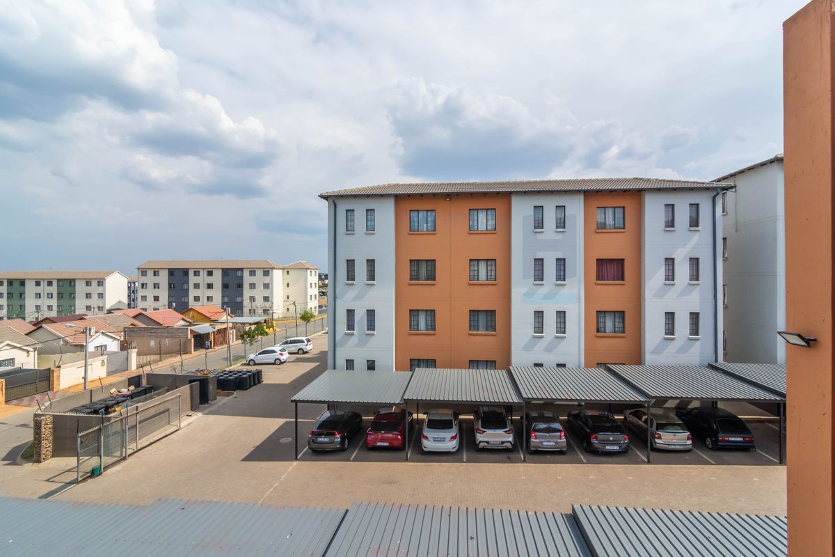 Aerial view of a townhouse complex featuring a paved parking area with covered carports and multi-story residential buildings.