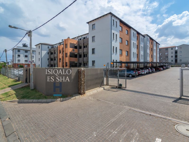 Front entrance view of a multi-story townhouse complex featuring paved driveway, secure gated access, and covered carport parking bays.