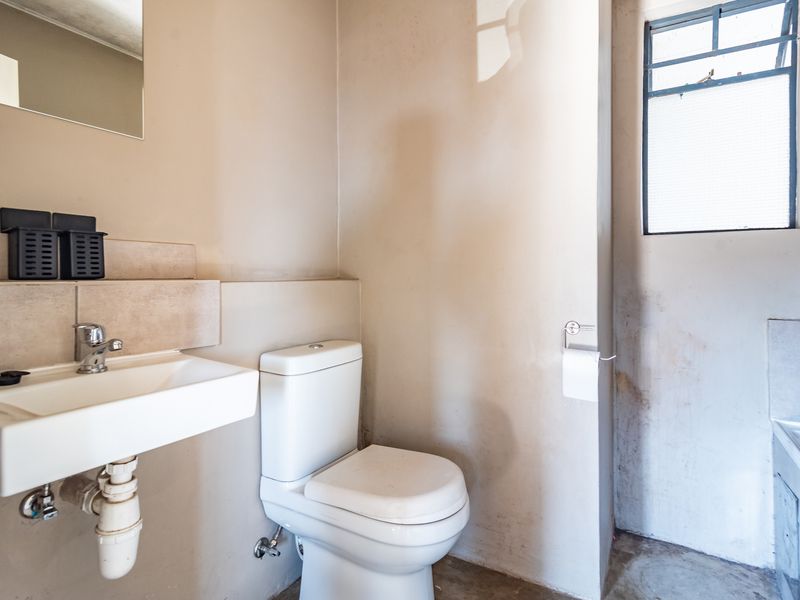 A compact bathroom featuring a wall-mounted basin and toilet, requiring cosmetic updates to the wall and floor finishes.