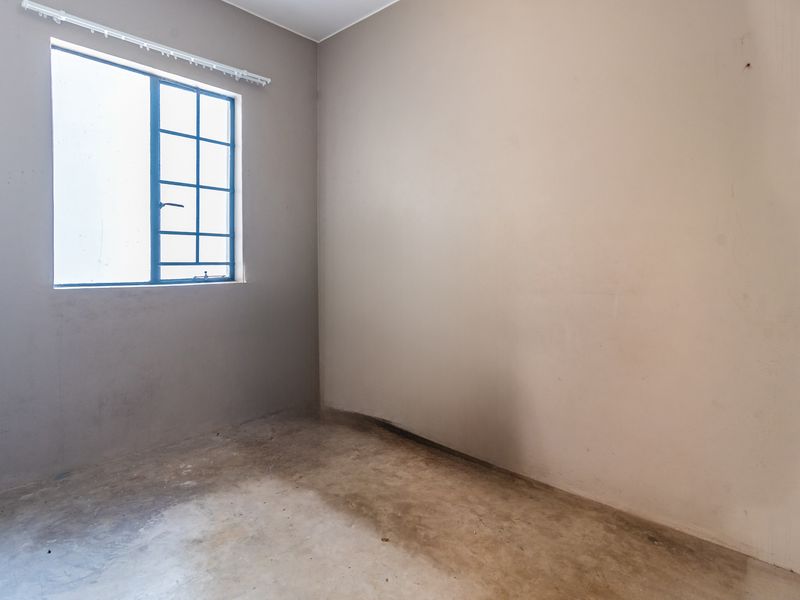 An empty, unfinished bedroom featuring a steel-framed window and bare concrete flooring, offering a blank canvas for renovation and interior design.