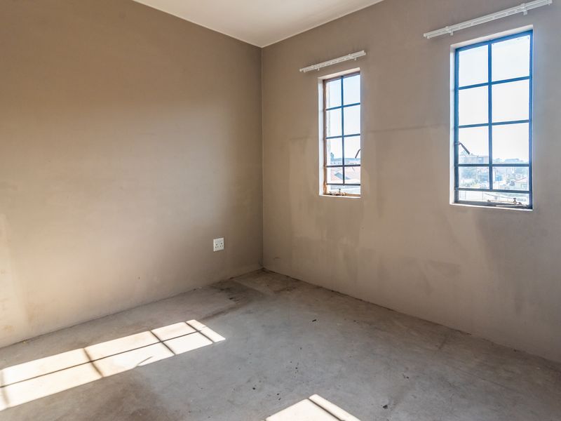 An empty bedroom featuring unfinished walls, exposed concrete flooring, and steel-framed windows, offering a blank canvas for renovation and interior design.
