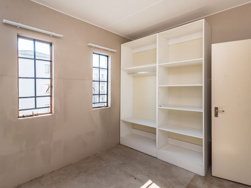 An empty bedroom featuring built-in shelving, steel-framed windows, and unfinished wall and floor surfaces, offering a blank canvas for renovation.