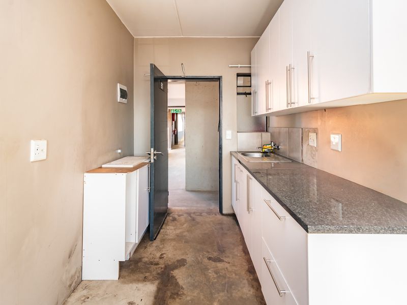 A compact kitchen area featuring white cabinetry, granite countertops, and a stainless steel sink, currently in need of flooring and wall finishing.