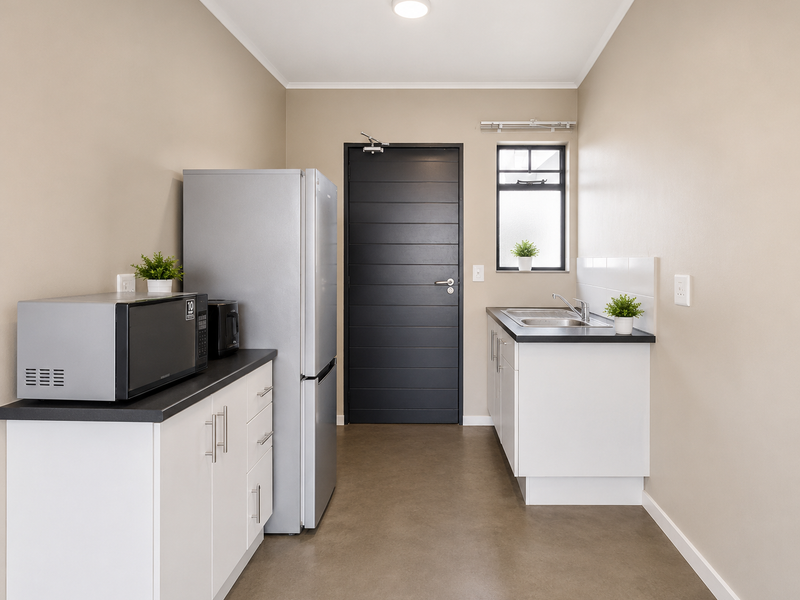 A clean and functional scullery featuring white cabinetry, dark laminate countertops, a stainless steel sink, and a modern dark-toned door.