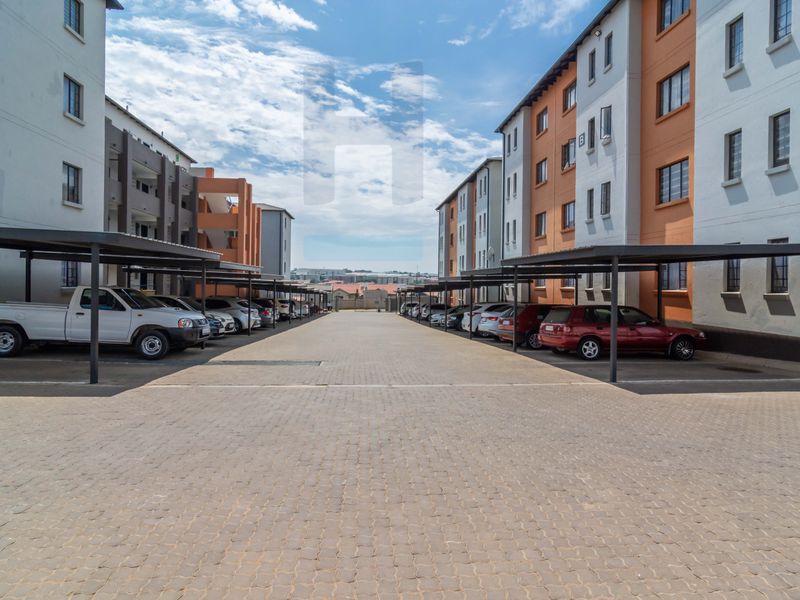 Exterior view of a townhouse complex featuring a paved driveway and covered parking bays between multi-story residential buildings.