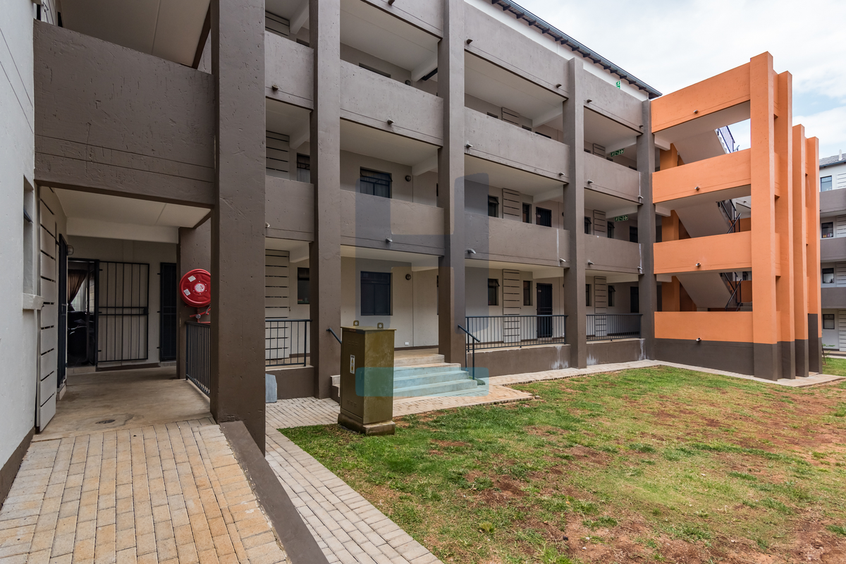 Exterior view of a multi-story townhouse complex featuring concrete staircases, metal railings, and a paved walkway leading to the building entrance.