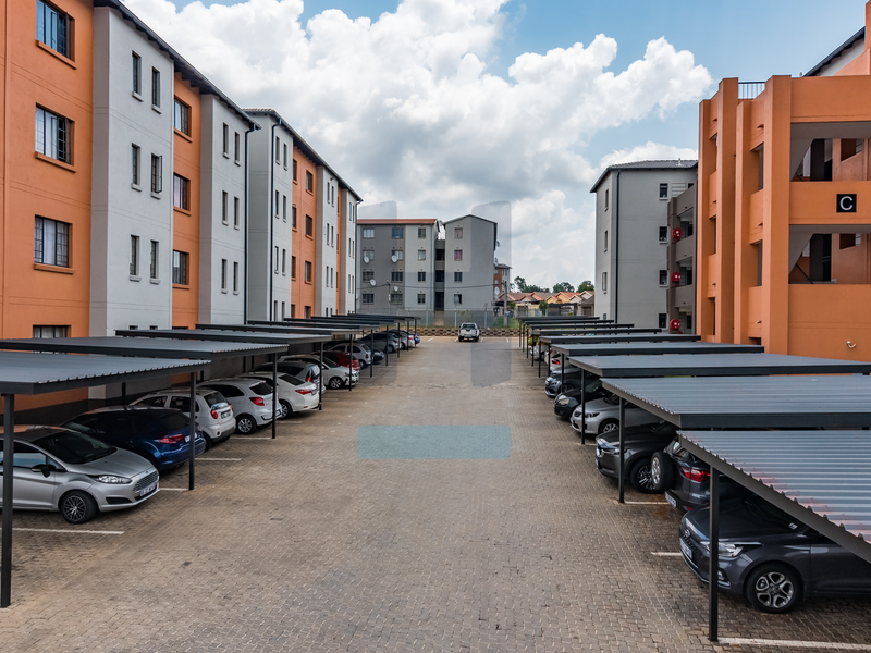 An aerial view of a townhouse complex featuring paved driveways and multiple rows of covered parking bays between residential apartment blocks.