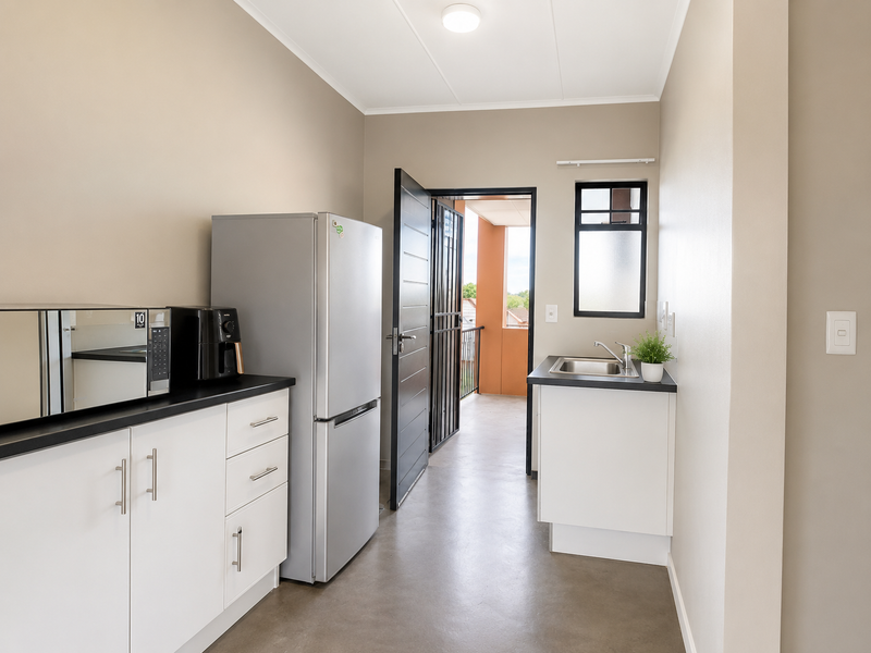 A functional scullery area featuring white cabinetry, dark countertops, a stainless steel sink, and direct access to an outdoor balcony.