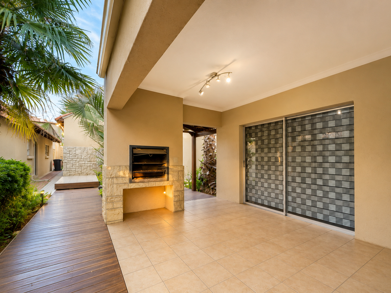 Covered patio area featuring a built-in braai with stone cladding, tiled flooring, and direct access to the home via sliding glass doors.